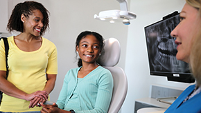 Young girl sitting in dental chair with her mother by her side, ready to talk with the dentist.