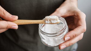 Individual holding a jar of baking soda and a toothbrush.
