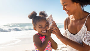 Cute little girl listening to shell at beach with her mom.