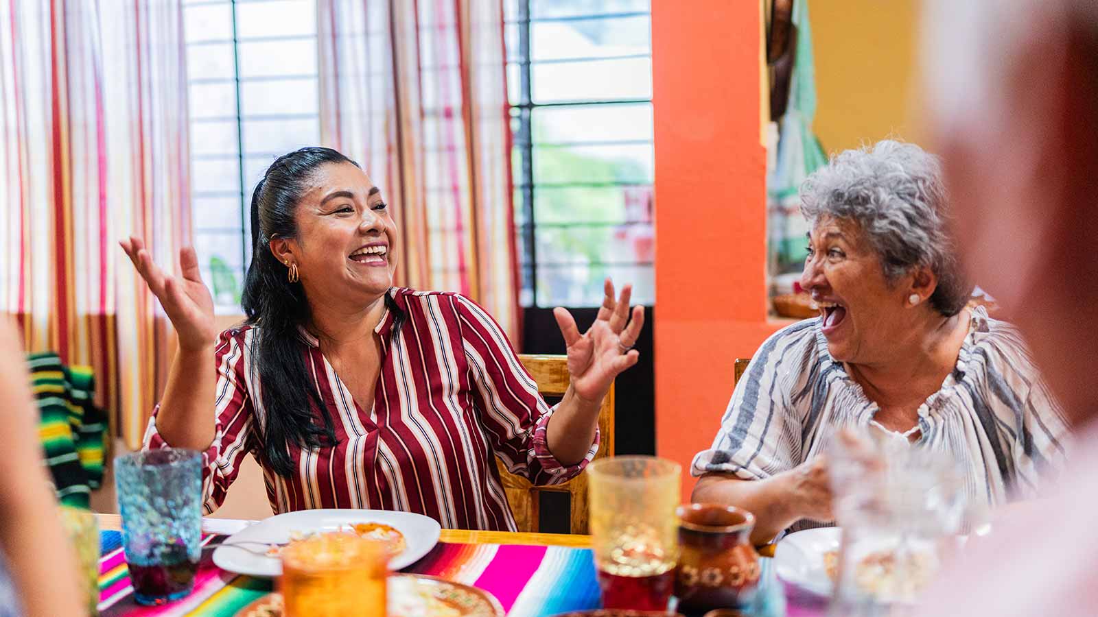 Woman smiling at dinner table with hands in the air.