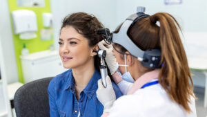 Eye doctor checking woman's ear using otoscope at medical clinic.