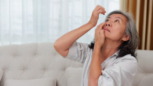 An elderly woman carefully using eye drops in her eyes.