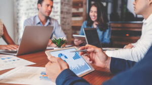 Associates sitting at a table with tablets and laptops, viewing charts and graphs on their devices.