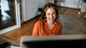 Cheerful young woman video conferencing on computer at home office