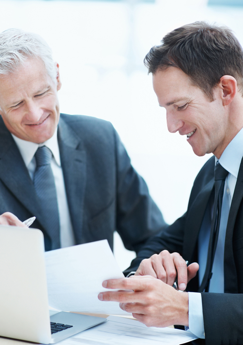 Two male colleagues sitting at a table with a laptop discussing business.