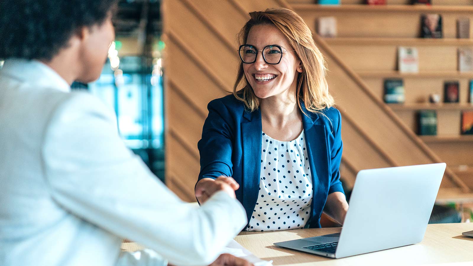Male and female sitting at a table with laptop, shaking hands.