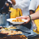 Individual with a plate of food going through a buffet line.