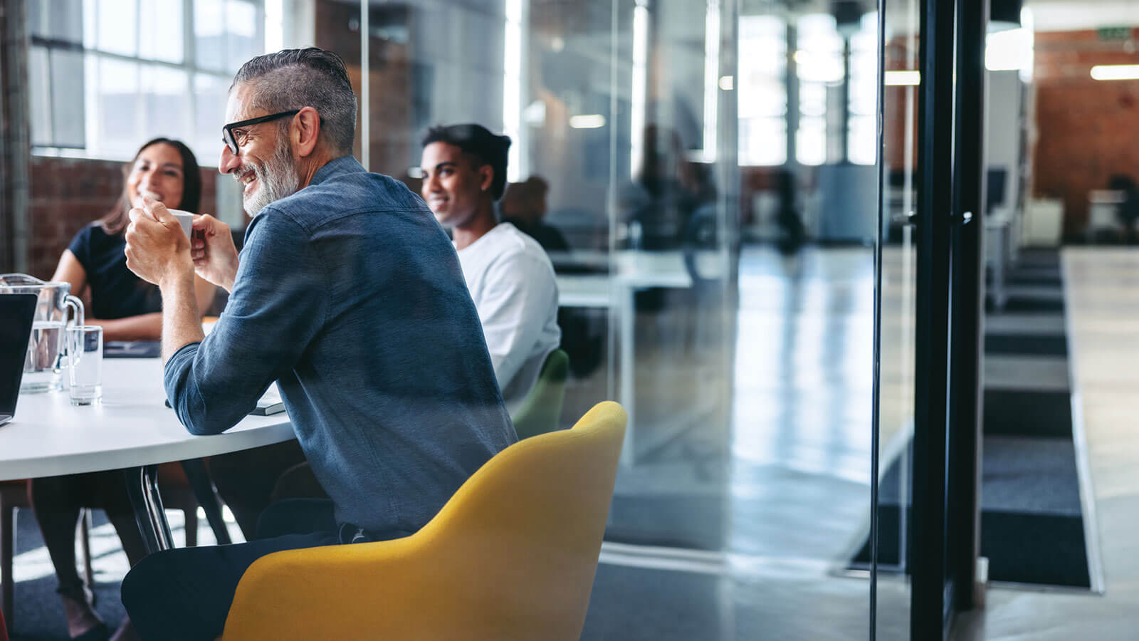 A group of smiling employees at a professional employer organization sit around a conference table discussing their pooled employer plan offering.