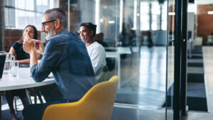 A group of smiling employees at a professional employer organization sit around a conference table discussing their pooled employer plan offering.