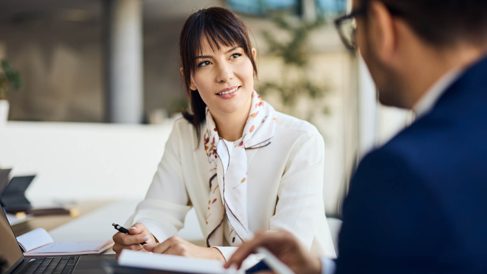 A professional woman working in a corporate office meets with her financial professional to discuss disability insurance to protect her income.