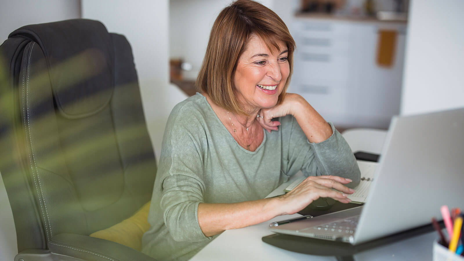Woman smiling while using laptop on her desk.
