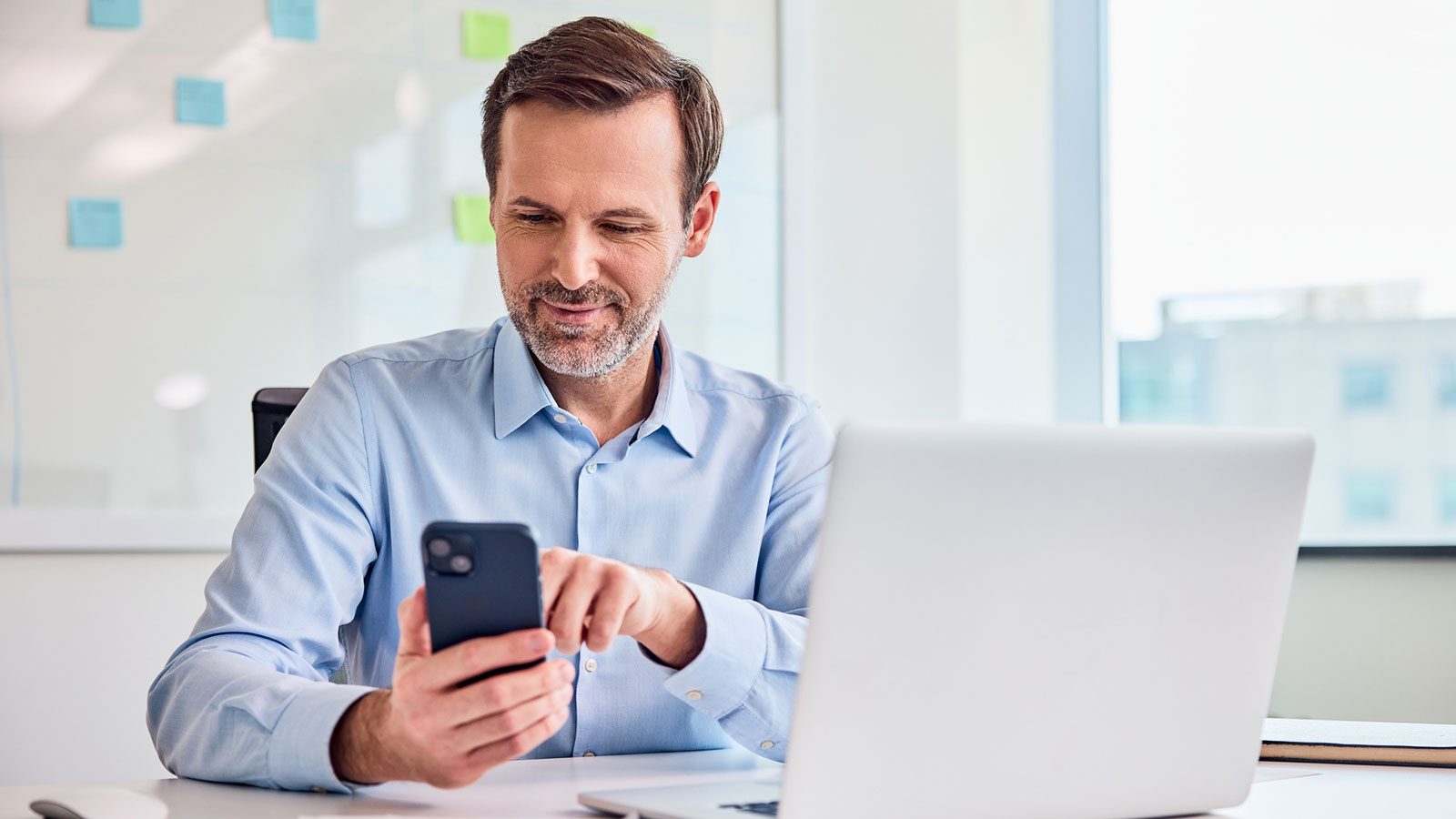 A financial professional sits at his office desk and checks social media best practices on his phone to help grow his business and engage clients.
