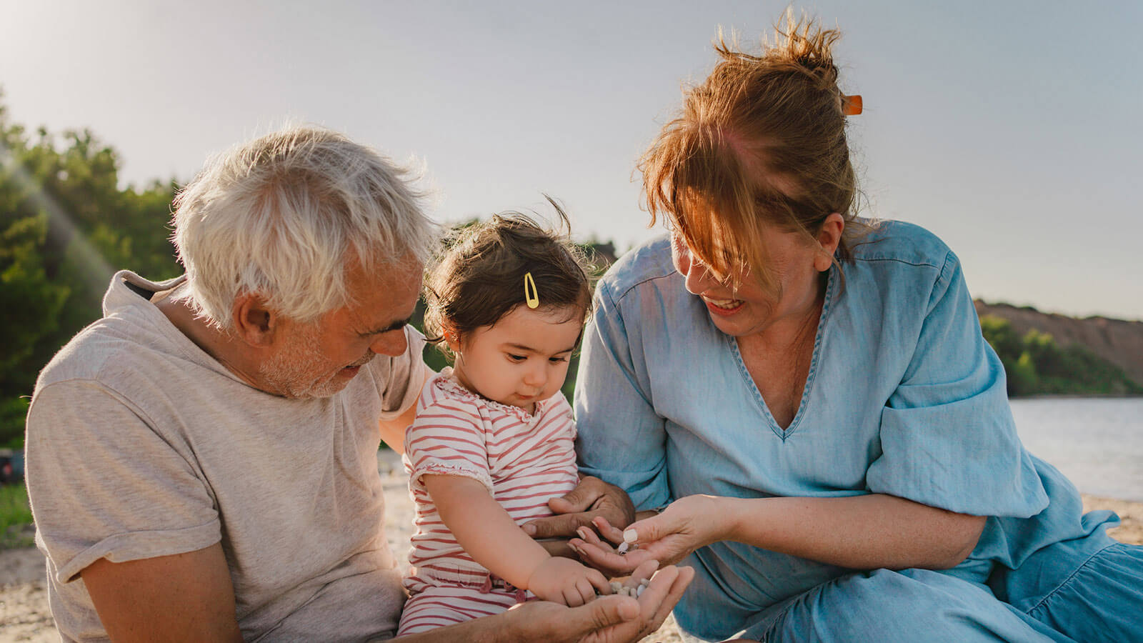 Grandparents happily play with their one-year-old granddaughter at the beach on a sunny day. Their proactive legacy planning will ensure their wealth is passed on to their granddaughter, and other family members, exactly as they wish.