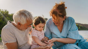 Grandparents happily play with their one-year-old granddaughter at the beach on a sunny day. Their proactive legacy planning will ensure their wealth is passed on to their granddaughter, and other family members, exactly as they wish.