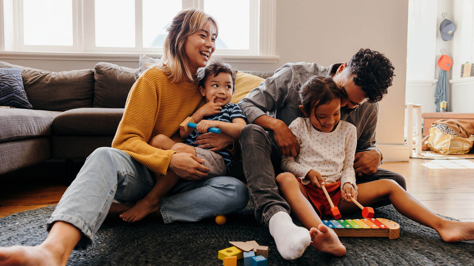 Family of four sitting on the floor in their home, playing, laughing and having a good time together.